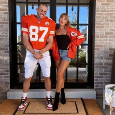 a woman standing next to a man in front of a door wearing an orange jersey