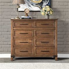 a wooden dresser sitting in front of a painting on a brick wall with a clock above it