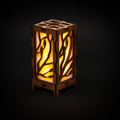 a small wooden lantern with an intricate design on the front and sides, lit up at night