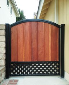 a wooden gate with black iron bars on the top and bottom part, in front of a house