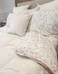 an unmade bed with white sheets and pink flowers on it, along with pillows