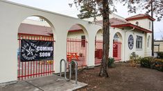 a white building with red iron gates and a sign on the door that says coming soon