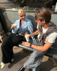 two people sitting on a bench drinking coffee