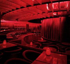 the interior of a restaurant with red lighting and tables, chairs, and curtains on the walls