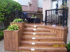 a wooden deck with planters on it and stairs leading up to the front door