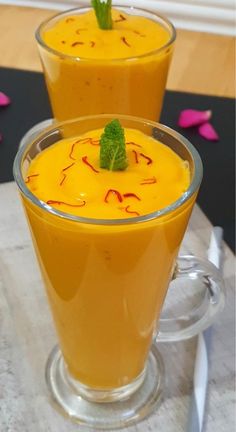 two glasses filled with orange liquid and garnished with green leaves on the rim