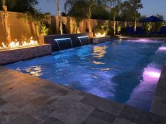 an outdoor swimming pool at night with fire lights on the side and palm trees in the background