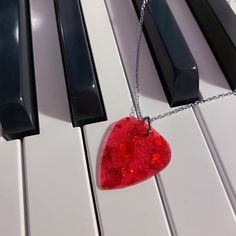 a red guitar pick sitting on top of a white piano keyboard with a chain attached to it