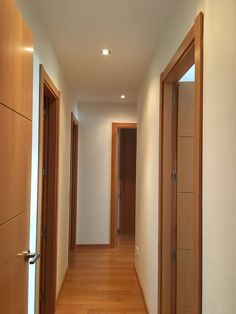 an empty hallway with wooden doors and hard wood flooring on both sides, leading to another room