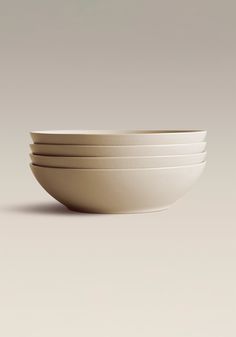 four white bowls stacked on top of each other in front of a gray background,