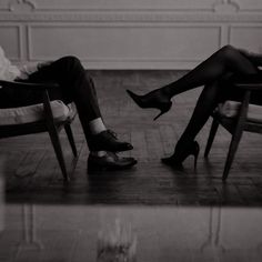 two people sitting in chairs with their feet on each other's legs and one person wearing high heeled shoes