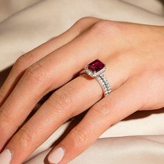 a woman's hand wearing a ring with a red stone in the center and diamonds around it