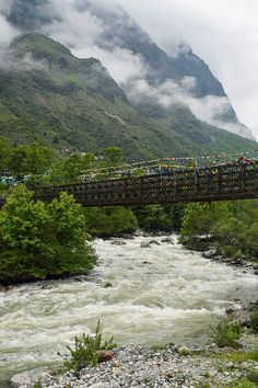 a bridge over a river with people on it and some mountains in the back ground