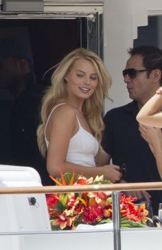 a woman in a white dress standing next to a man on a boat looking at her cell phone