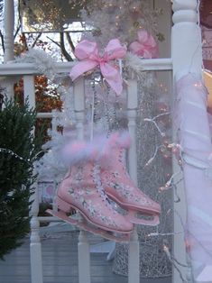 some pink boots are hanging from a white pole with christmas lights on the porch behind them