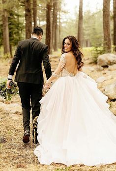 a bride and groom walking through the woods holding hands