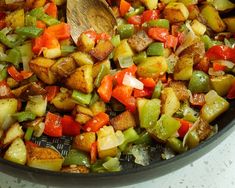 a pan filled with potatoes and peppers on top of a counter next to a wooden spoon