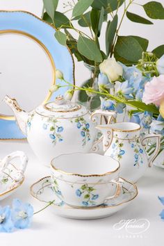 a tea set with blue and white flowers in front of a plate, bowl, and mirror