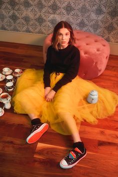 a woman is sitting on the floor in a yellow tulle skirt and black shirt