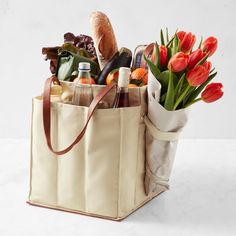 a tote bag filled with wine, bread, and flowers sitting on a table