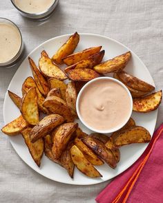 a white plate topped with french fries next to two cups of dipping sauce on a table