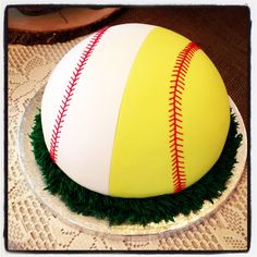 a cake decorated with green grass and a baseball on it's side, sitting on top of a doily