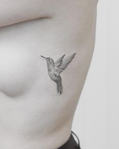 a small bird tattoo on the side of a woman's right breast, which is black and white