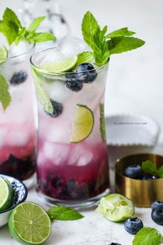 two glasses filled with blueberry mojitas and mint garnished with lime