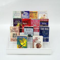 a white book rack filled with books on top of a white table next to a wall