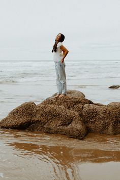 a woman standing on top of a rock near the ocean