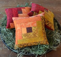 three orange and red pillows sitting on top of a black bowl filled with green grass