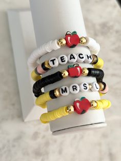 a stack of bracelets that say teach and have apple charms on them, sitting next to a white wall