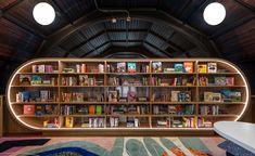 a room with bookshelves and a bathtub in the center, surrounded by rugs