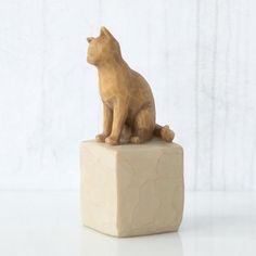 a cat figurine sitting on top of a block of wood with white background