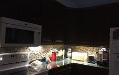 a kitchen with black cabinets and white appliances in the middle of it is lit up at night