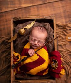 a baby in a harry potter outfit is holding a wand and wearing glasses while sitting in a wooden box