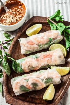 shrimp rolls on a wooden platter with lime wedges and dipping sauce in the background