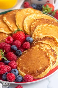 pancakes with berries and blueberries on a plate next to oranges, raspberries and strawberries