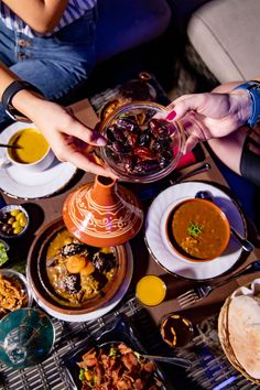 people sitting at a table filled with plates and bowls full of different types of food