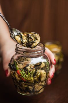 a woman holding a spoon full of food in a glass jar with other items inside