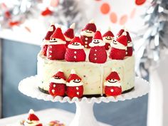 a white cake with strawberries on top and santa clause decorations around the edges is sitting on a table