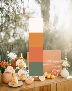 an orange and green color scheme is displayed on a wooden table with vases, flowers and fruit