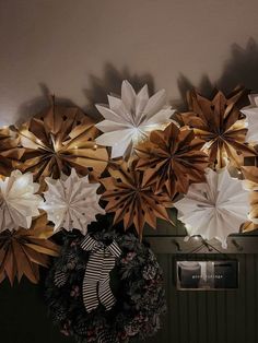 a bunch of paper flowers are hanging on the wall above a wreath with lights around it