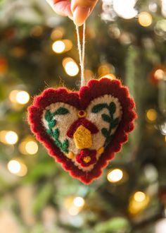 someone is holding a heart ornament in front of a christmas tree