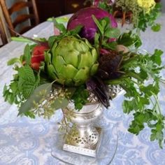 an arrangement of flowers in a silver vase on a table with blue and white cloth