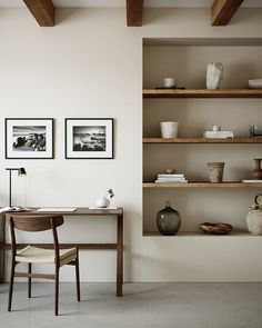 a desk and chair in a room with shelves on the wall above it, along with two vases