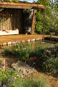 an outdoor area with flowers, rocks and a wooden structure in the background that is surrounded by greenery