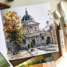 a drawing of a building on top of a table next to some markers and pencils