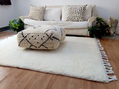 a white couch sitting on top of a wooden floor next to a rug covered in black and white pillows