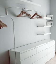 an empty room with white furniture and clothes hanging on the wall, including two hangers